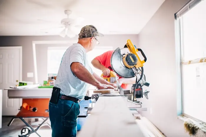 A contractor cutting trim with a miter saw in a room being remodeled